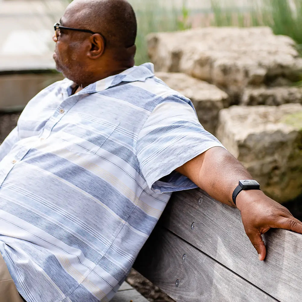 Man in a striped shirt sitting on a bench outdoors with a Belle W watch.