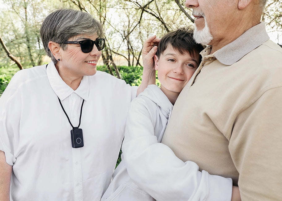 Two older adults and a child outdoors with a Belle S device on the woman's chest.