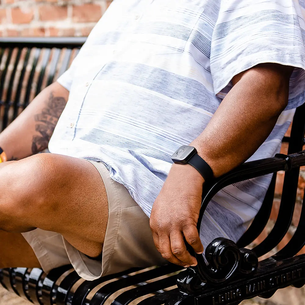 Person sitting on a bench wearing a striped shirt and beige shorts, with a Belle W watch on their wrist. 